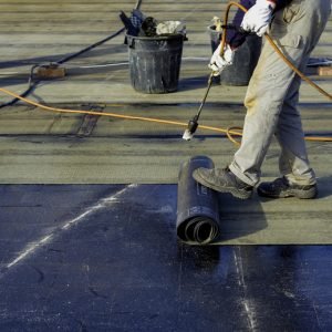 Worker preparing part of bitumen roofing felt roll for melting by gas heater torch flame. On the back of the sheath there is the stamp "Made in Italy" product